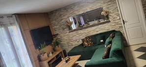 Ein Wohnzimmer mit Steinsandsteinwand, einem grünen Sofa, einem Holztisch und einem Wand-Fernseher.