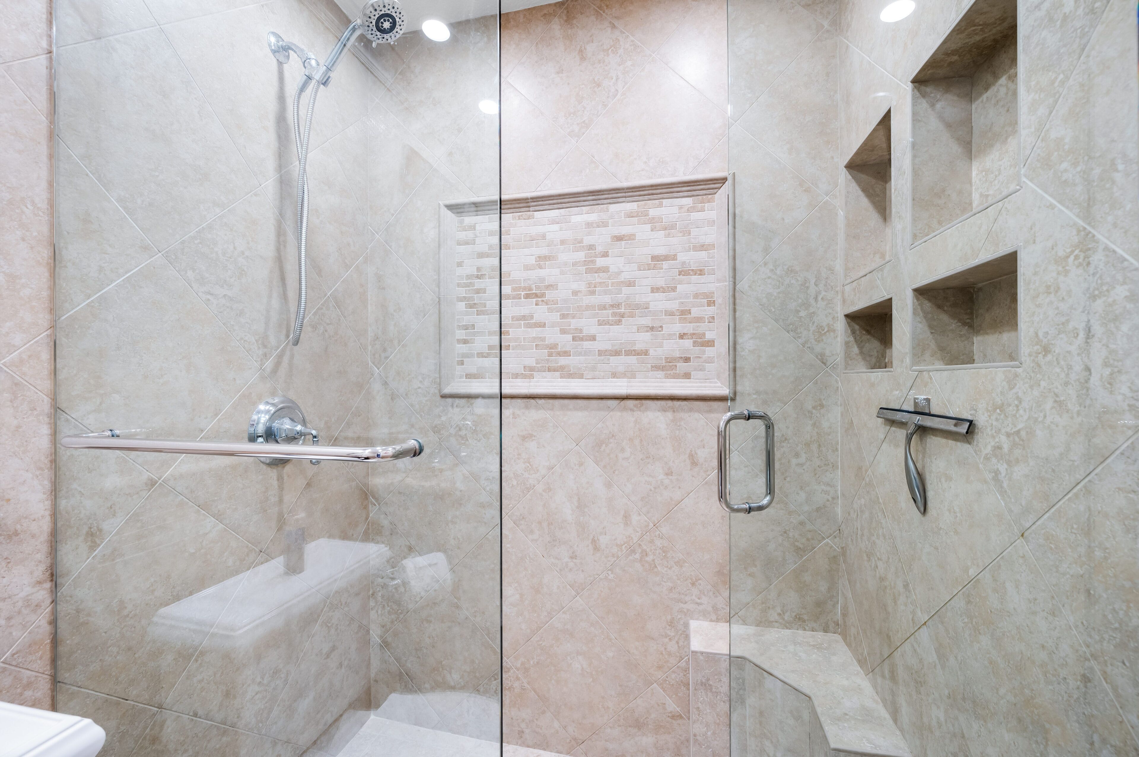 A modern bathroom with a glass shower enclosure, a handrail, a toilet, and a sink.