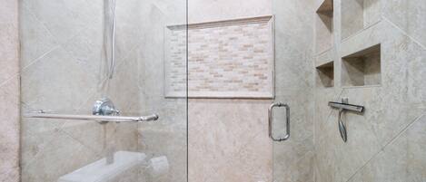 A modern bathroom with a glass shower enclosure, a handrail, a toilet, and a sink.