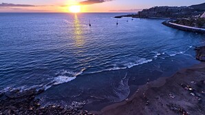 Vista al tramonto sulla costa, con una spiaggia rocciosa e una passeggiata.