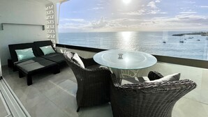 Un balcone con un divano e poltrone in vimini, affacciato su una marina con barche e cielo sereno.
