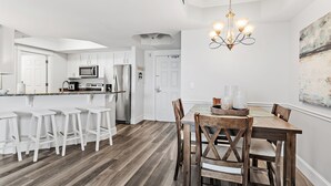 A kitchen with white cabinets, a stainless steel refrigerator, and a bar area with white stools. - ~St. Lucia 702~ Sleeps 6 ~ Gulf View~ (Destin)