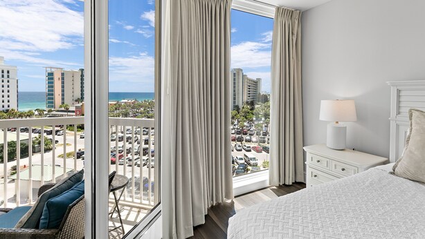 A hotel room with a balcony, a bed, a nightstand, and a view of the cityscape and ocean. - ~St. Lucia 702~ Sleeps 6 ~ Gulf View~ (Destin)