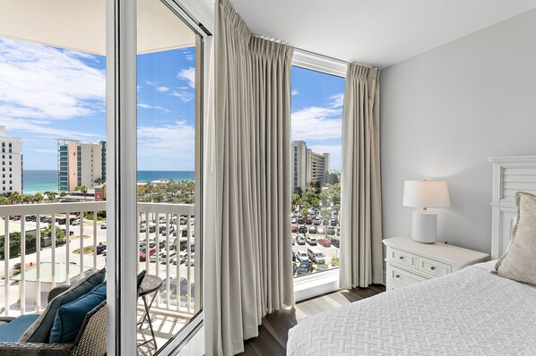 A hotel room with a balcony, a bed, a nightstand, and a view of the cityscape and ocean.