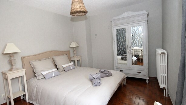Une chambre avec un grand lit, deux tables de chevet avec des lampes, une armoire et un radiateur.
