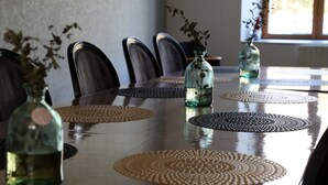 Une table à manger dotée d’un plateau réfléchissant, entourée de chaises, et agrémentée de sets de table en fibres tressées et de vases en verre contenant des fleurs séchées.