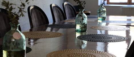 A dining table with a reflective surface, surrounded by chairs, and adorned with woven placemats and glass vases with dried flowers.
