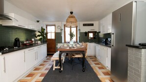 Une cuisine moderne avec des meubles blancs, une table à manger avec des chaises, un luminaire suspendu et un réfrigérateur.