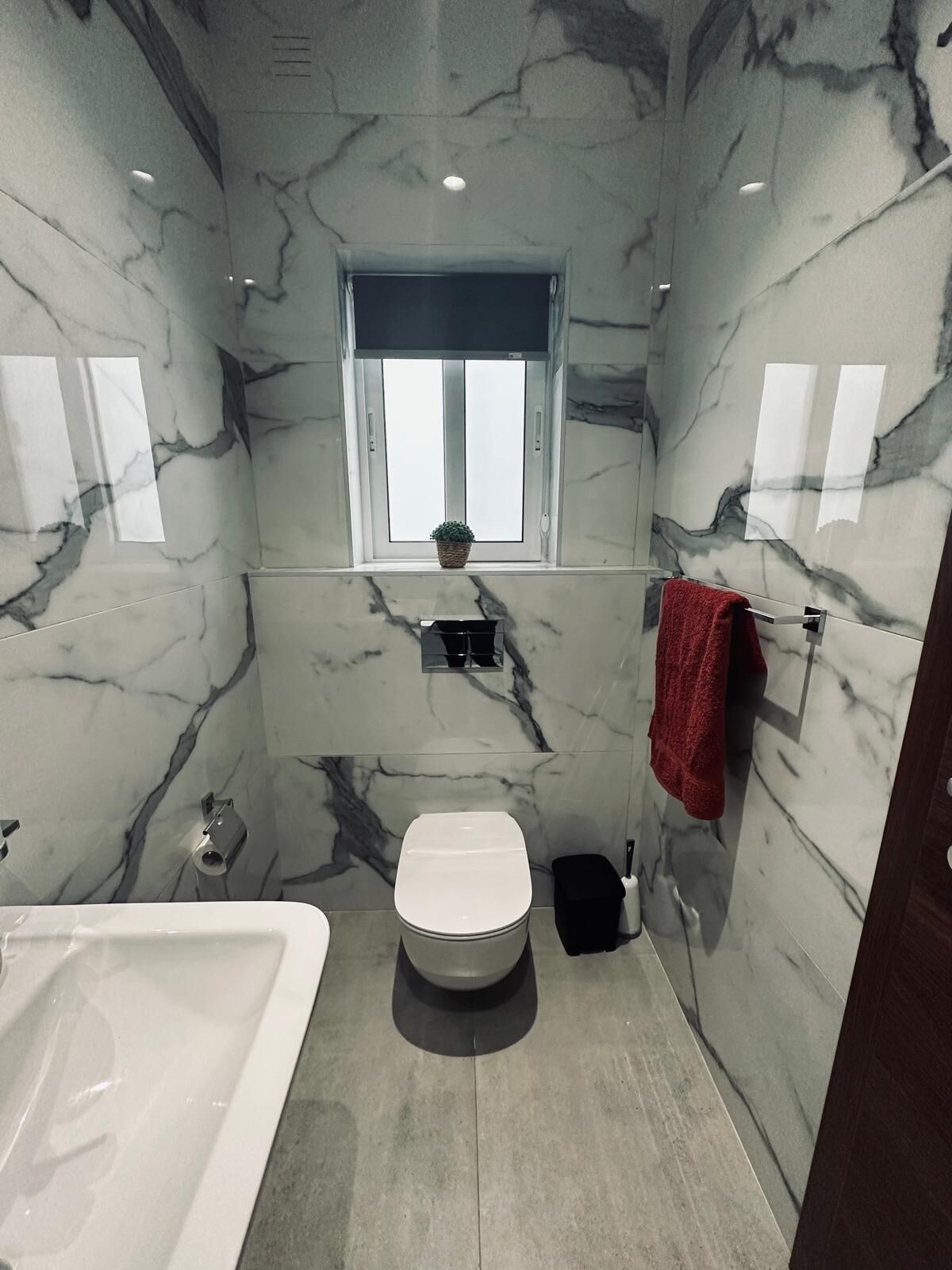 A bathroom with a marble wall, a window, a toilet, a bathtub, and a red towel.