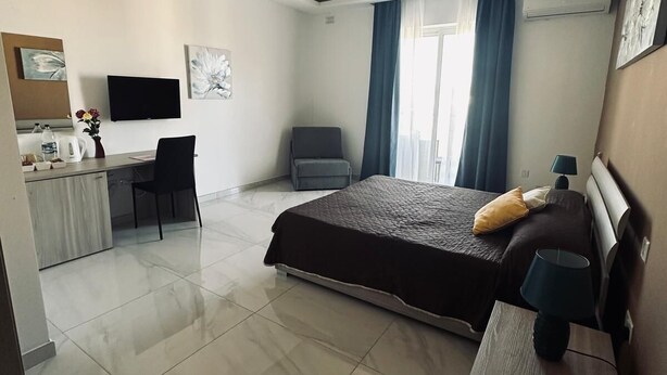 Une chambre d’hôtel moderne équipée d’un lit, d’un bureau, d’une chaise, d’une télévision et d’une fenêtre avec des rideaux.