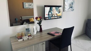 Une chambre d’hôtel avec un bureau en bois, un téléviseur fixé au mur, un vase avec des fleurs et un magazine.