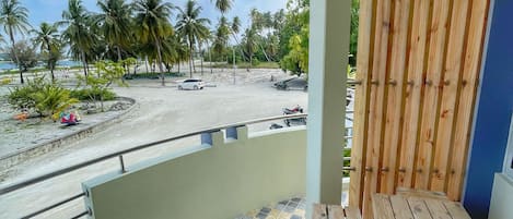 A balcony with a tiled floor, wooden furniture, and a view of a beach with palm trees.