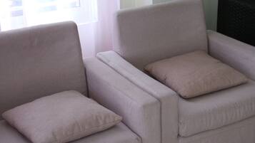 Dos sillones con cojines en una habitación con una ventana y un mueble oscuro al fondo.