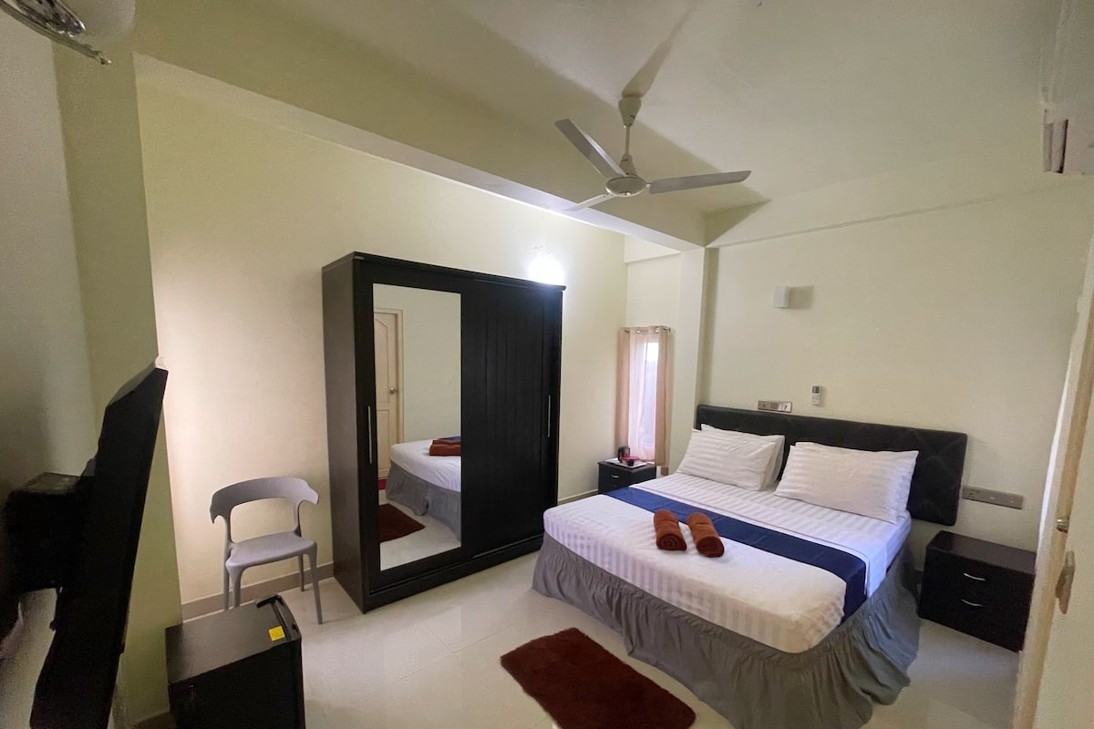 A bedroom with a bed, a desk, a chair, a wardrobe, and a ceiling fan.