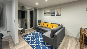 A modern living room with a grey sofa, blue patterned rug, and wooden flooring. - A lovely modern annexe nestled in the village of Guilsfield. (Guilsfield)