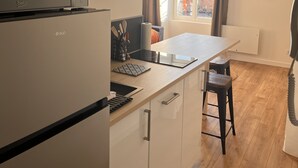 A compact kitchen with a built-in microwave, a small island with a tablet, and a window with curtains. - Appartement Élégant (Angoulême)