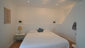 A modern bedroom with a large bed, a bedside table, a wall-mounted fan, and a small plant on the nightstand.