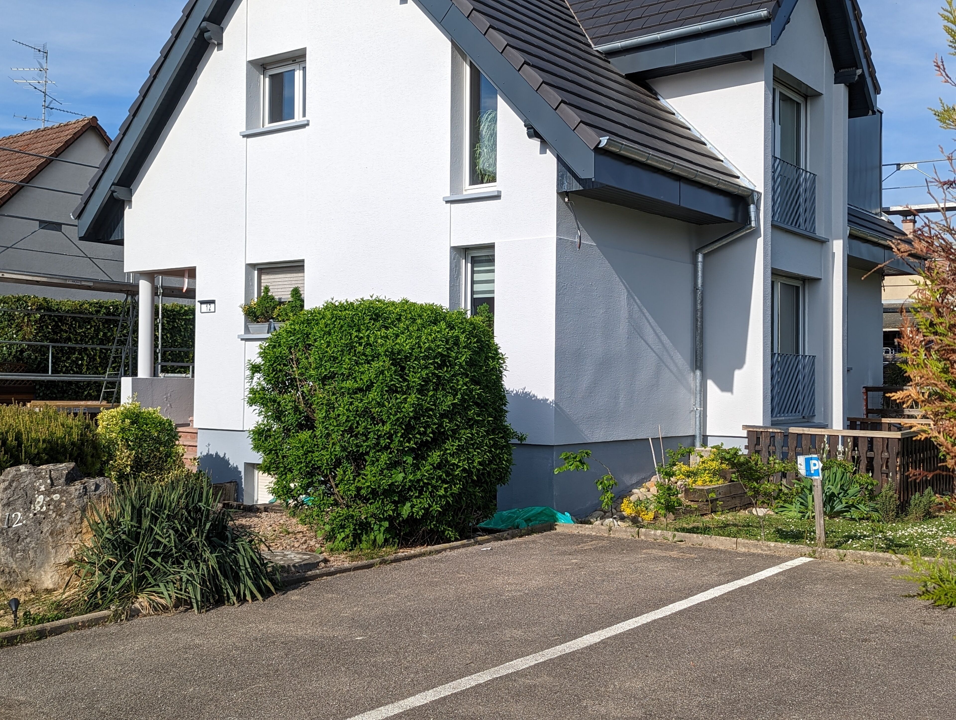 Een modern herenhuis met twee verdiepingen, een witte gevel, een grijs dak en een klein balkon.