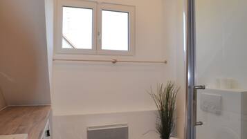 Een moderne badkamer met een glazen douchecabine, een raam boven de wastafel en een houten vloer.