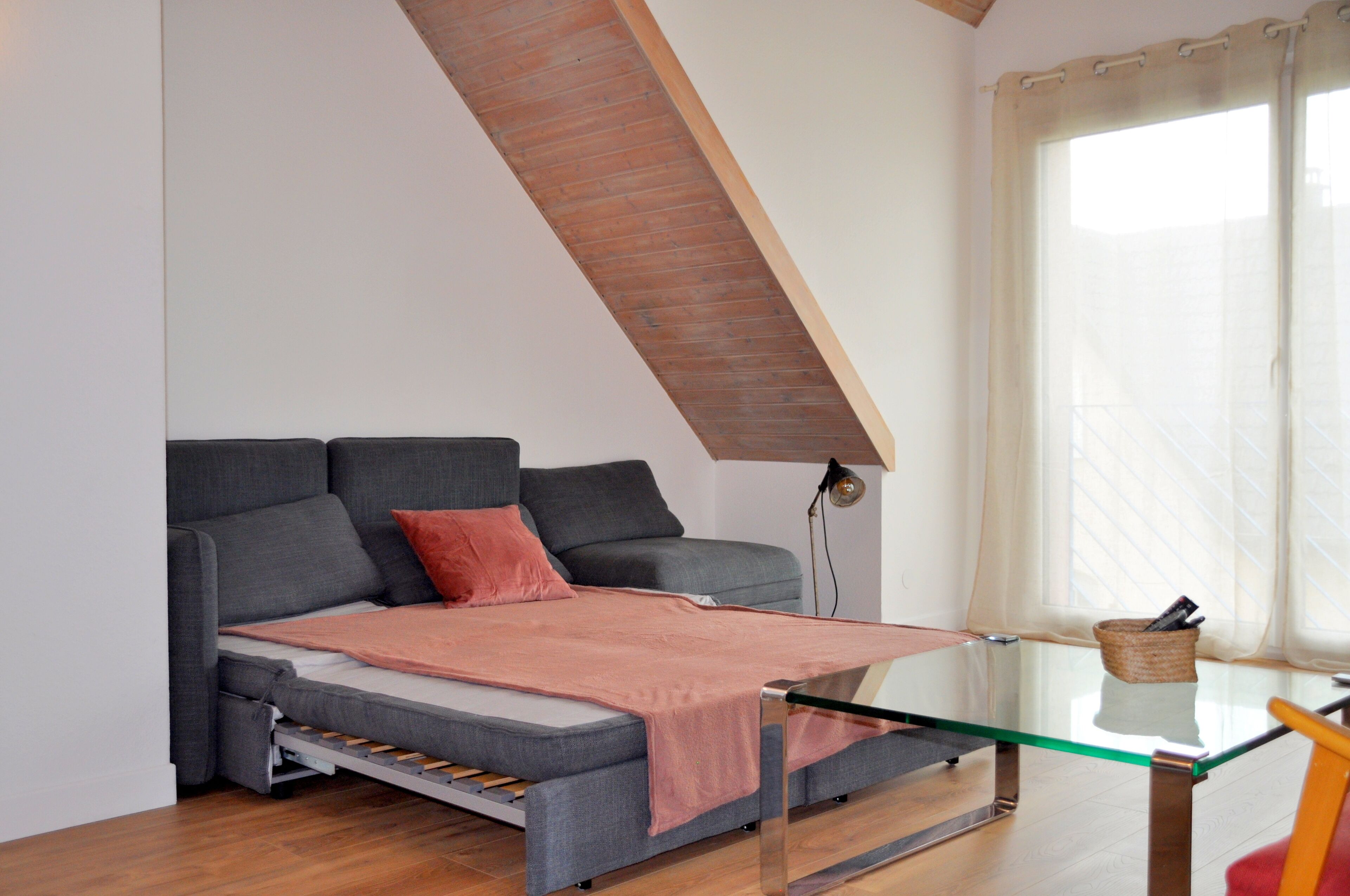 Une pièce de style loft avec un canapé-lit, une table basse en verre et une fenêtre avec des rideaux.