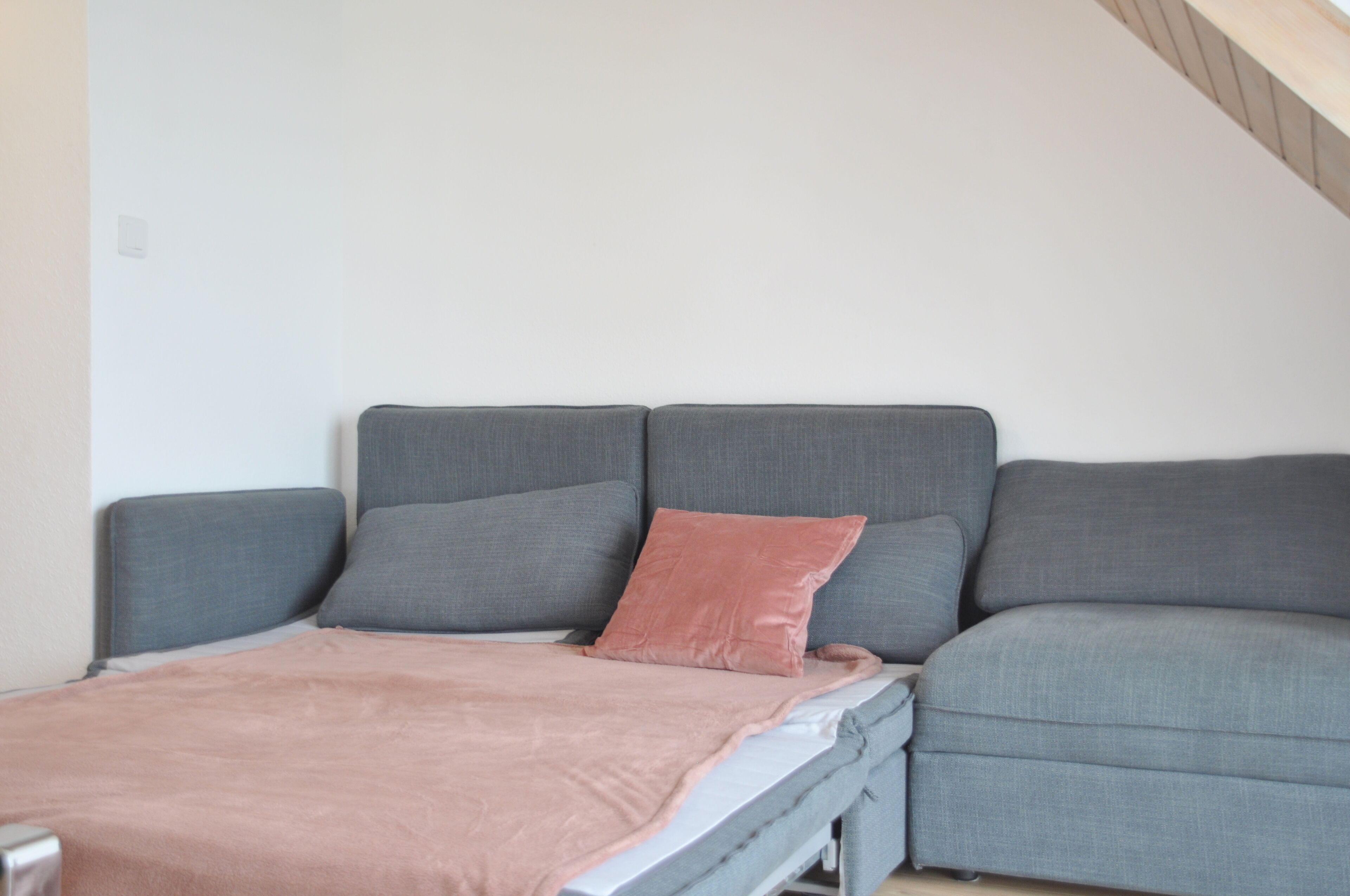 A modern, compact room with a grey sofa bed and a single pink pillow.