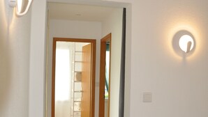 A hallway with a wooden floor, white walls, and a potted plant.