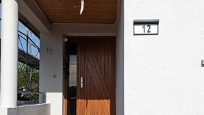 A modern building entrance with a wooden door, numbered 12, and a set of stone steps leading up to it.