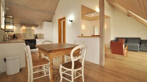 A spacious living area with a wooden dining table and chairs, a grey sofa, and a kitchen in the background.
