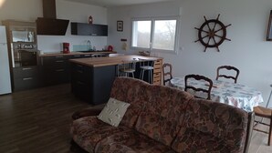 Een moderne keuken met een centraal eiland, een zithoek met een tafel en stoelen, een bank en een decoratieve stuurwiel aan de muur.