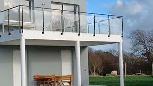 Een modern, twee verdiepingen hoog gebouw met een balkon, een houten bankje en een gazon.