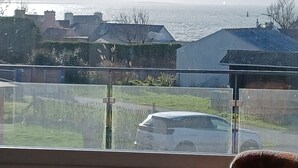Een woonwijk met huizen, een auto en uitzicht op zee.