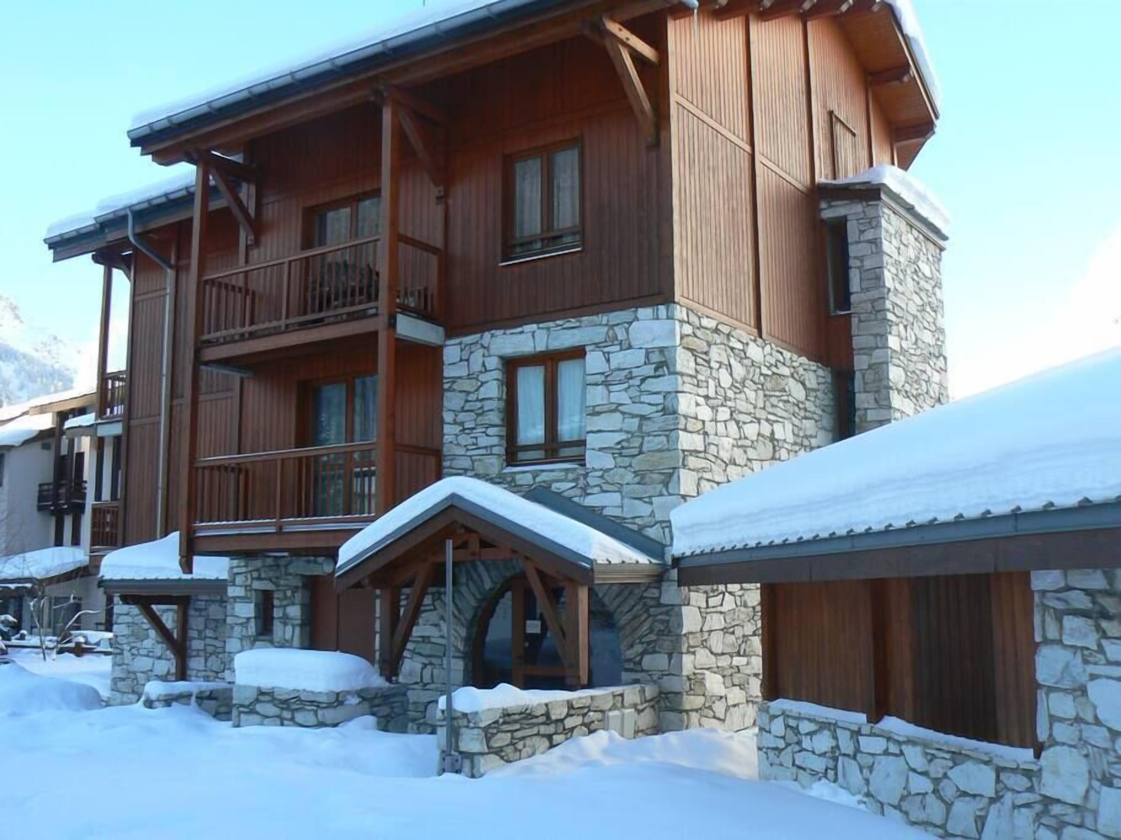 A multi-story lodge with stone and wood construction, balconies, and a snow-covered roof.