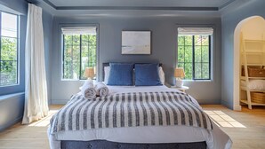 Een slaapkamer met een groot bed, twee ramen, een schilderij aan de muur en een witte kledingkast.