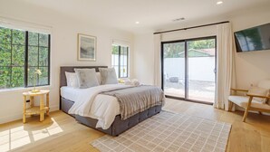 Een moderne slaapkamer met een groot bed, een aan de muur bevestigde televisie en een schuifdeur naar een buitenruimte.