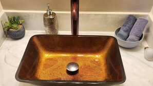 Une cuisine avec un évier rectangulaire en cuivre, une petite plante en pot, un bol décoratif et un porte-serviette.