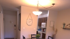 Un salon avec un canapé gris, une table à manger avec des chaises, un coin cuisine et un couloir.