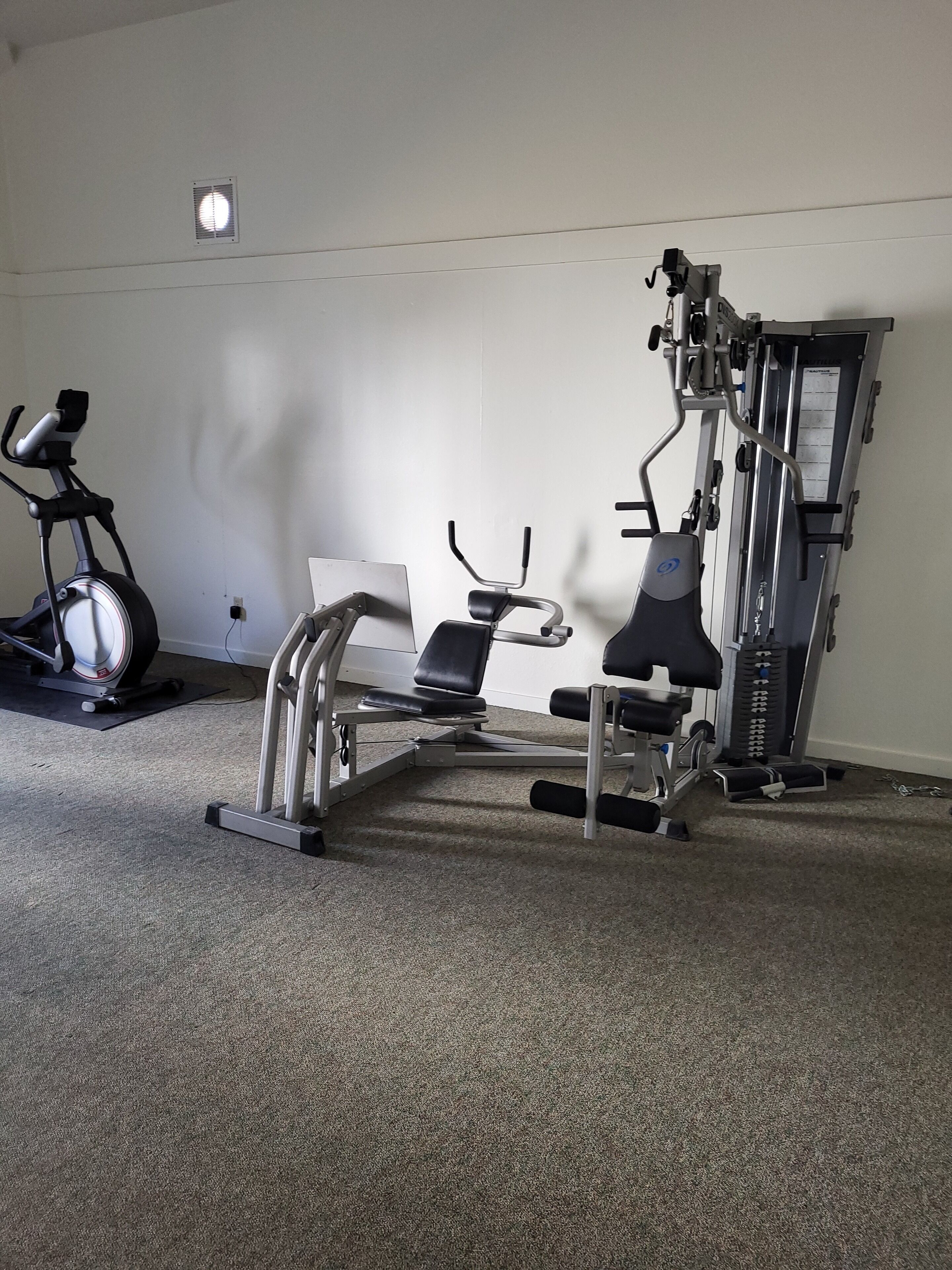 A gym with exercise equipment including a stationary bike, a bench press, and a weight machine.