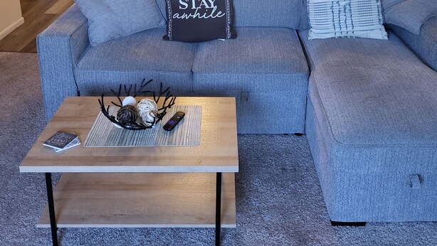 Un salon avec un canapé d’angle gris, une table basse en bois et, au fond, un coin repas.