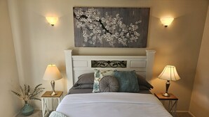 Une chambre à coucher comprenant un lit, deux tables de chevet, une lampe fixée au mur et un élément décoratif mural.