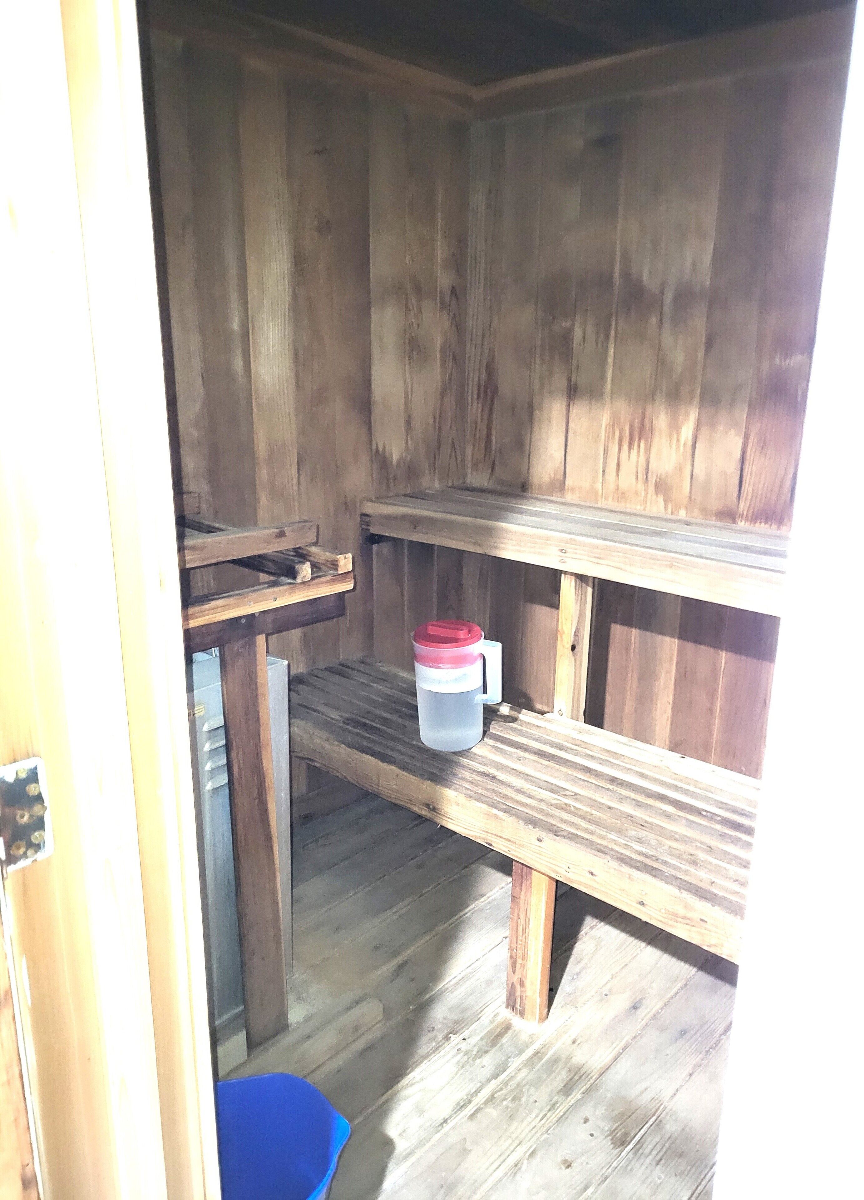 A rustic wooden cabin interior with a bench, a small table, and a blue bucket.