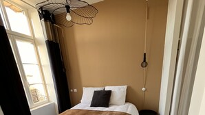 A bedroom with a bed, a hanging light fixture, and a window with curtains. - Charmant Appartement (Angoulême)