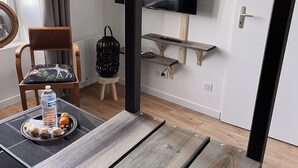 A modern living room with a wooden table, a chair, a TV mounted on the wall, and a small shelf. - Charmant Appartement (Angoulême)