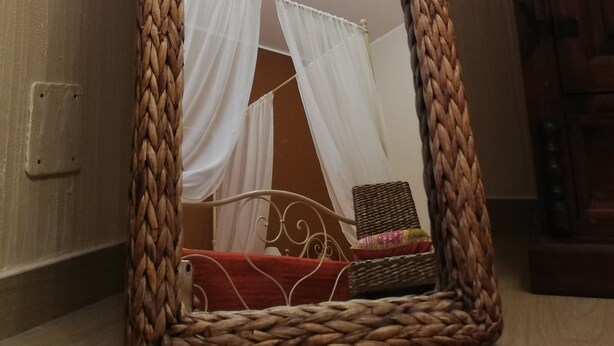 Un espejo con marco trenzado en una habitación que tiene una cama, cortinas y muebles de madera.
