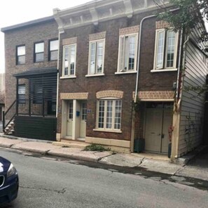 Un bâtiment en briques de deux étages, doté d’un porche à l’avant, d’une porte de garage et d’un petit jardin devant.