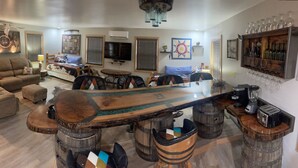 A living room with a unique bar area featuring a wooden table and bar stools. - Whiskey Barrel Bunkhouse (Sunrise Beach)