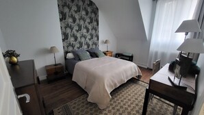 Ein Schlafzimmer mit einem Bett, zwei Nachttischen, einem Schminktisch, einer Lampe, einer Kommode, einem Spiegel und einem gemusterten Teppich.