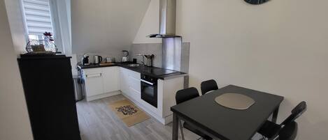 A compact kitchen with a dining area, a black refrigerator, a stove, and a clock on the wall.