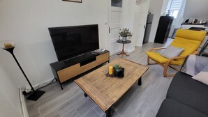 Ein modernes Wohnzimmer mit Flachbildfernseher, Couchtisch aus Holz, gelbem Sessel und einem kleinen Beistelltisch mit Pflanze.