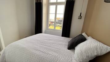 Une chambre avec un grand lit, une fenêtre avec des rideaux et une vue sur un bâtiment à l’extérieur.