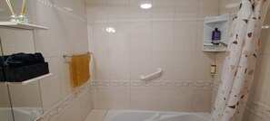 Une salle de bain équipée d’une baignoire, d’une douche, d’un porte-serviettes et d’une étagère pour les articles de toilette.